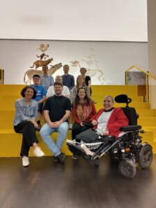 Alle Kollegen aus dem Büro auf einem Foto. Wir sitzen auf einer großen gelben Treppe. Hinter uns sind Kunstwerke von den Bremer Stadtmusikanten.