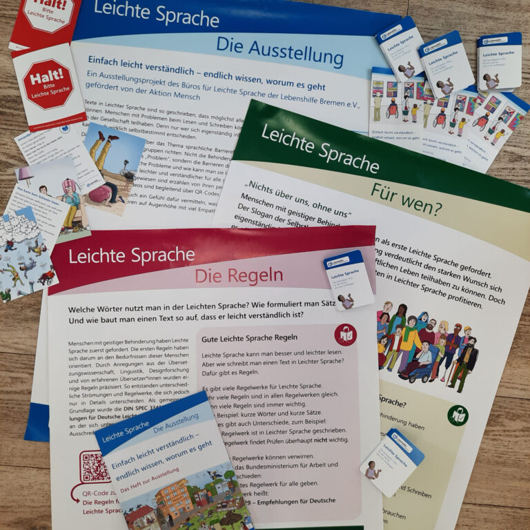 verschiedene Materialien für eine Ausstellung zur Leichten Sprache liegen auf dem Boden: Plakate, Faltposter, Rote Karten, Bildkarten und ein Heft zur Ausstellung
